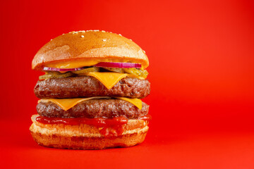 Delicious burger with double beef and cheddar cheese on a red background. Tasty fresh unhealthy burgers with cheese and two patties. Fast food, unhealthy food concept.