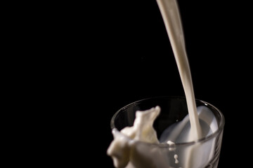 pouring milk in a glass. splash of white liquid isolated on dark background