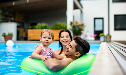 Young family with small daughter in swimming pool outdoors in backyard garden.