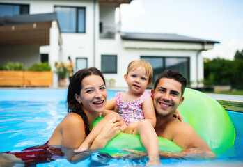Young family with small daughter in swimming pool outdoors in backyard garden.