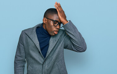 Young african american man wearing business clothes and glasses surprised with hand on head for...