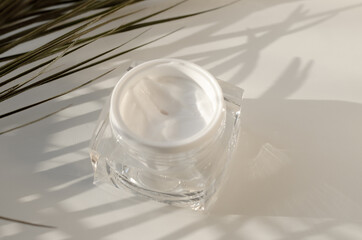 An open jar of cream on a light background with palm twigs. Skin care concept