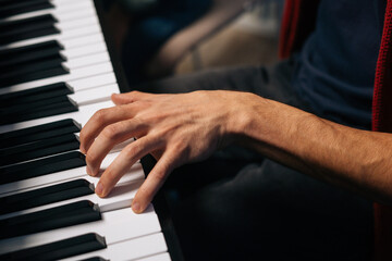 Obraz premium Top view of unrecognizable musician man playing on synthesize at home studio during lesson. Close-up hands of pianist male playing on digital piano in living room. Concept of music education.