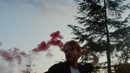 Guy with smoke bomb walking in mountains at sunset. Man waving smoke grenade