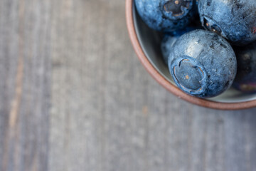 Top view of a group of wet dark blueberries, in bowl, on wooden table, horizontal, with copy space