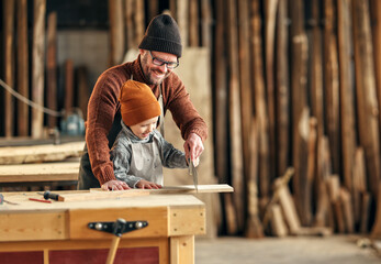 Happy kid with dad cutting wood in workshop