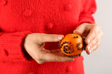 Woman decorating fresh tangerine with cloves, closeup. Making Christmas pomander ball