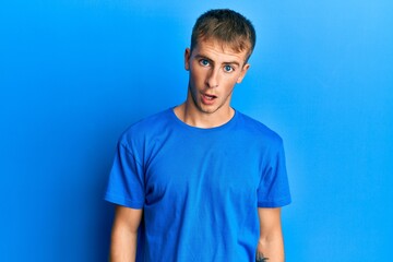 Young caucasian man wearing casual blue t shirt in shock face, looking skeptical and sarcastic, surprised with open mouth