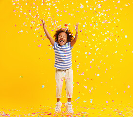 Excited African American kid jumping and catching confetti in studio