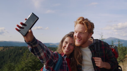 Positive woman and man taking selfie on smartphone during hike in mountains