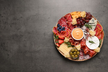 Wooden plate with different delicious snacks on grey table, top view. Space for text