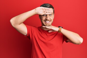 Handsome caucasian man wearing casual red tshirt smiling cheerful playing peek a boo with hands showing face. surprised and exited