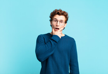 young handsome boy with mouth and eyes wide open and hand on chin, feeling unpleasantly shocked,...
