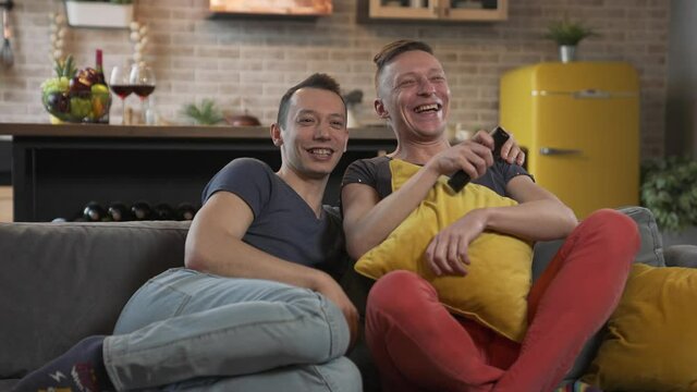 Male gay couple sitting on the couch and watching TV
