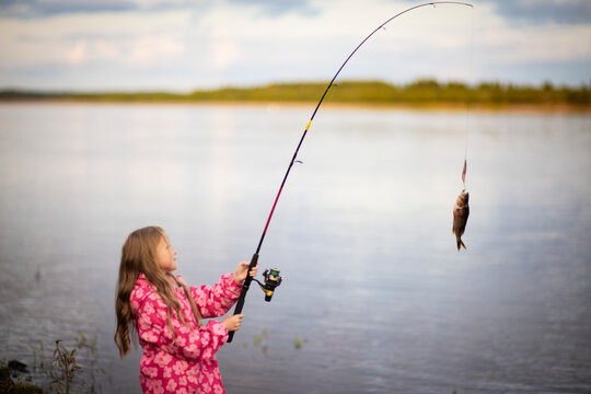 a girl is fishing. A lonely happy little kid is fishing on the river bank with a text space. Photos of children pulling a fishing rod while fishing at the weekend, Selective focus