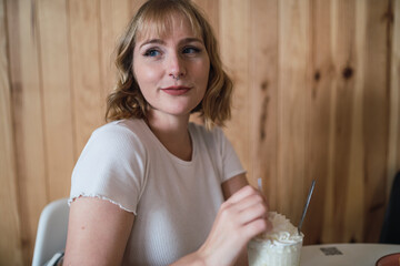 Chica joven rubia atractiva tomando batido y sonriendo en cafeteria