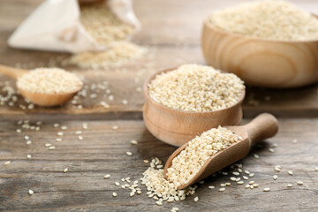 Bowl and scoop with sesame seeds on wooden table. Space for text