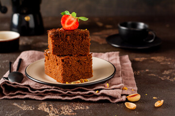 Stack of pieces or bar of chocolate cake brownie with strawberries and pistachio nuts on the black background, selective focus image