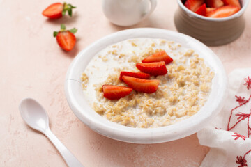 Oatmeal porridge with strawberries in a white plate on a linen napkin on pink background. Breakfast health food concept. Top view
