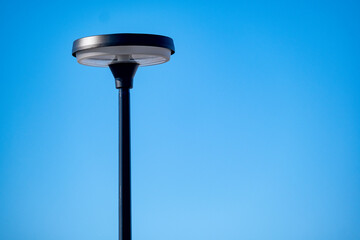 A closeup of a modern metallic street lamp against bright blue sky.