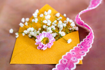 Obraz na płótnie Canvas scena matrimoniale con una busta riempita di fiori bianchi, un fiore lilà e un nastro rosa. auguri. invito