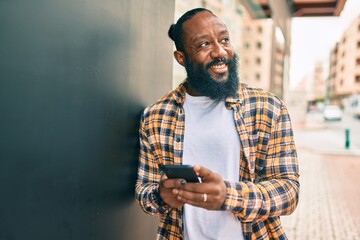 African american man with beard using smartphone typing and texting at the street with a happy smile