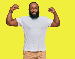 Young african american man wearing casual white tshirt showing arms muscles smiling proud. fitness concept.