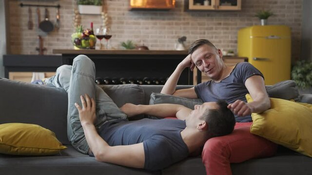 Cute male gay couple spend time together. They sit on couch and chat