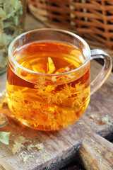 Linden herbal tea with flowers in a glass cup on wooden rustic board with lime blossom dry herb nearby, closeup, drink for relaxation, mental health,  naturopathy, homeopathy and folk medicine concept