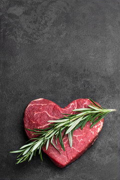 Heart shape raw fresh beef steak with rosemary stick on metal background