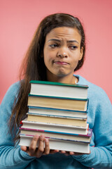 Bored african woman is dissatisfied with amount of homework and books. Lady is annoyed, discouraged frustrated by studies. Pink studio background 