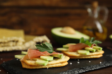 Delicious crackers with avocado, prosciutto and parsley on slate board, closeup