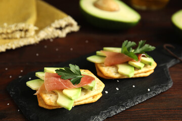 Delicious crackers with avocado, prosciutto and parsley on wooden table, closeup