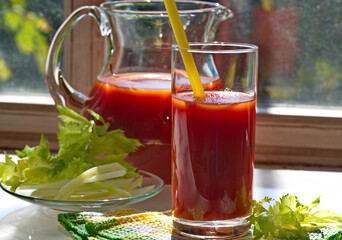 Freshly prepared tomato juice with a celery branch in two glasses stands on the kitchen table by the window. Detox snack. Horizontally.
