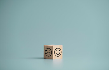 Smile face and sadness face print screen of two side of wooden cube block on blue background,...