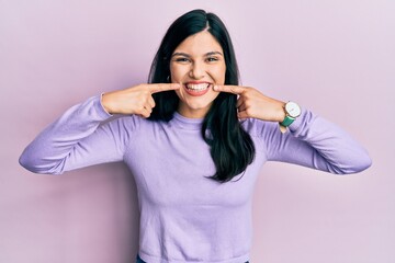 Fototapeta premium Young hispanic woman wearing casual clothes smiling cheerful showing and pointing with fingers teeth and mouth. dental health concept.