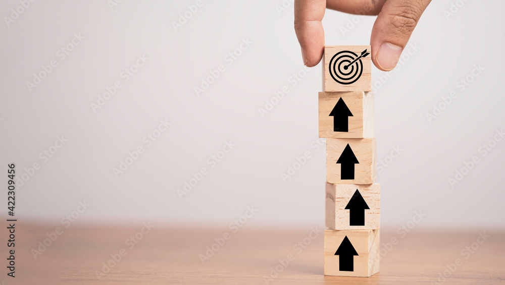 Poster hand putting target board on up arrows which print screen on wooden cube block, increasing and chall