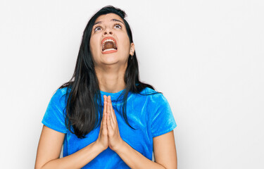 Young hispanic woman wearing casual clothes begging and praying with hands together with hope...