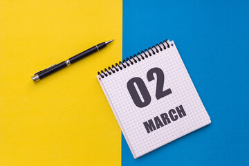 March 2nd. Day of 2 month, calendar date. A notebook with a spiral and a pen lies on a yellow-blue background, flat lay, copy space