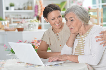 mother and daughter sitting at table with laptop, at home