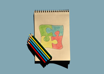Autism awareness day or month. The drawn puzzle is colored in different colors as a symbol of autism awareness. Sketchbook and pencils for children's creativity.