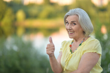 Happy senior woman with thumb up in the park