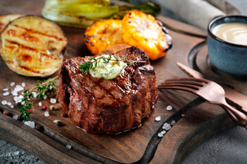 Grilled beef tenderloin steak on a wooden board with butter and thyme. Filet Mignon recipe with...