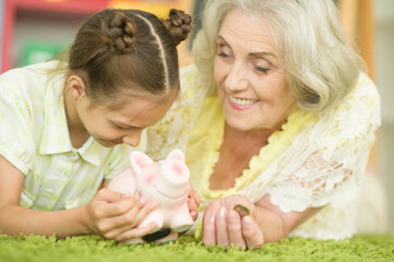 Obraz na płótnie Canvas Happy grandmother and granddaughter with piggy bank