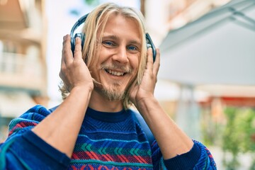 Young scandinavian student man smiling happy using headphones at the city.