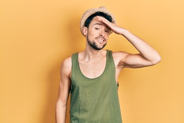 Young hispanic man wearing summer hat surprised with hand on head for mistake, remember error....