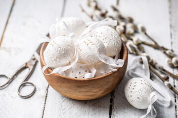 Handmade white easter eggs with willow catkins in a wooden bowl on wooden table