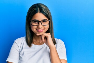 Obraz na płótnie Canvas Young latin woman wearing casual clothes and glasses smiling looking confident at the camera with crossed arms and hand on chin. thinking positive.