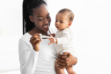 Happy young African American mother looking at thermometer