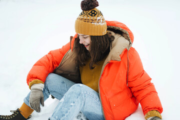 Young  woman in orange jacket sitting on the ground after a fresh snow fall